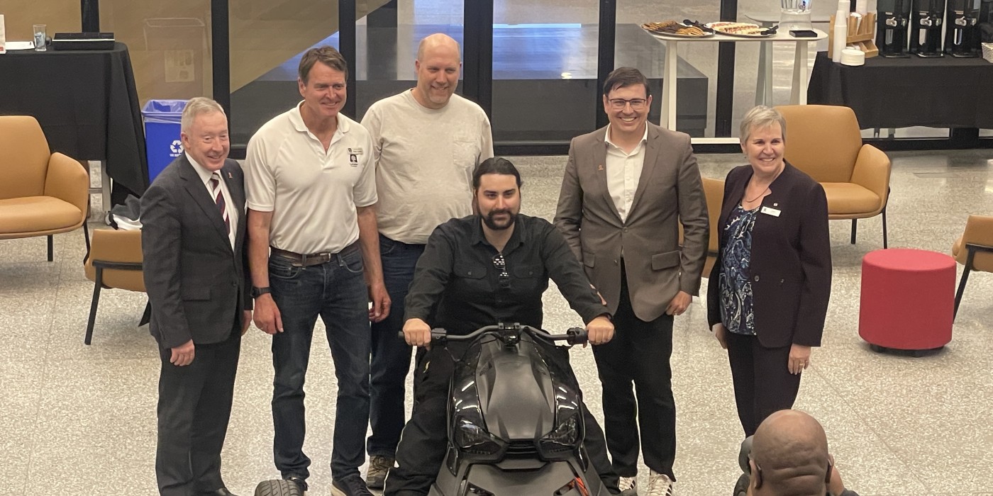 Six people work together to pull off a tarp to unveil a three-wheel black trike