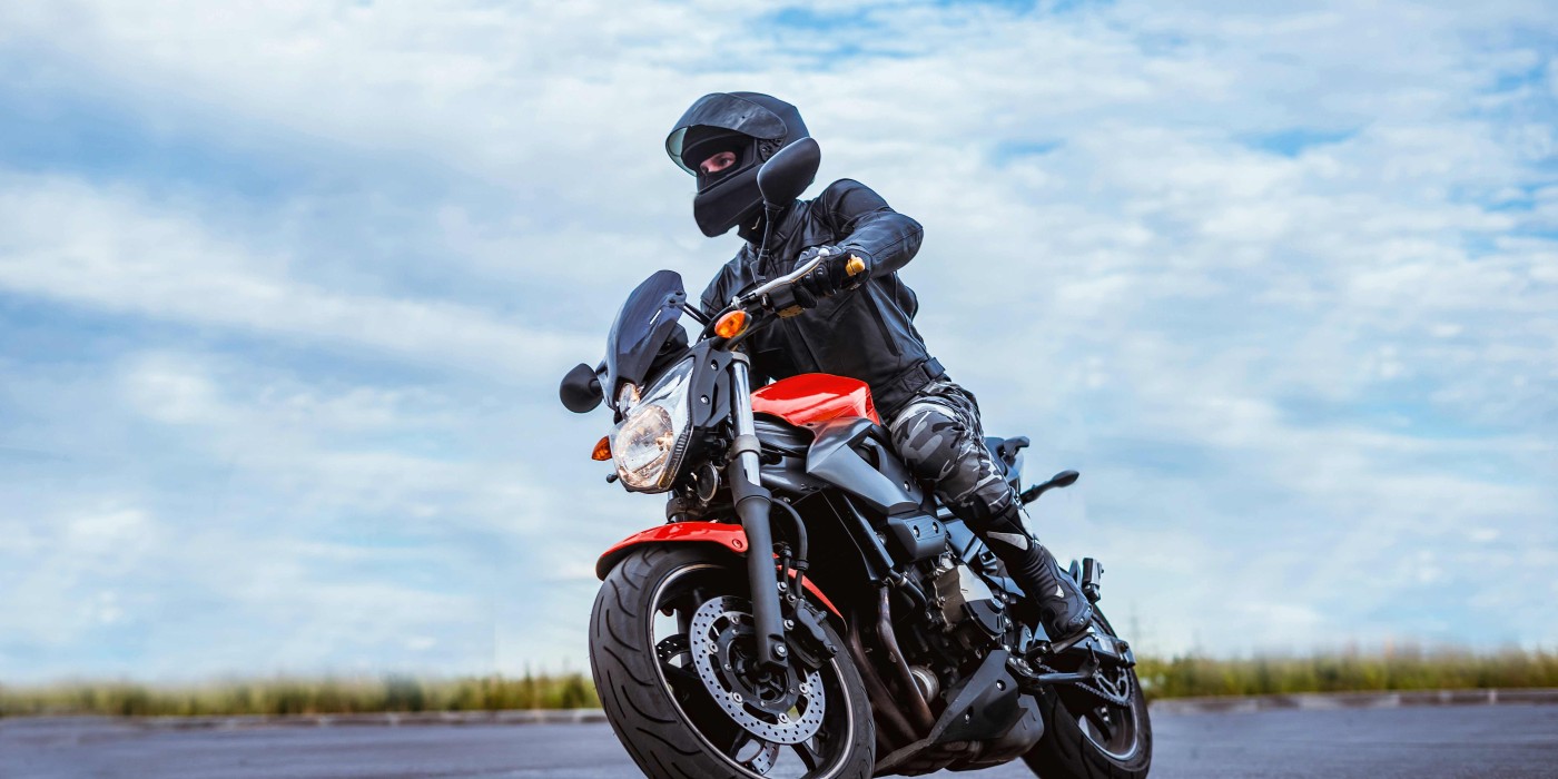 A person in black riding a red motorcycle on a cloudy day