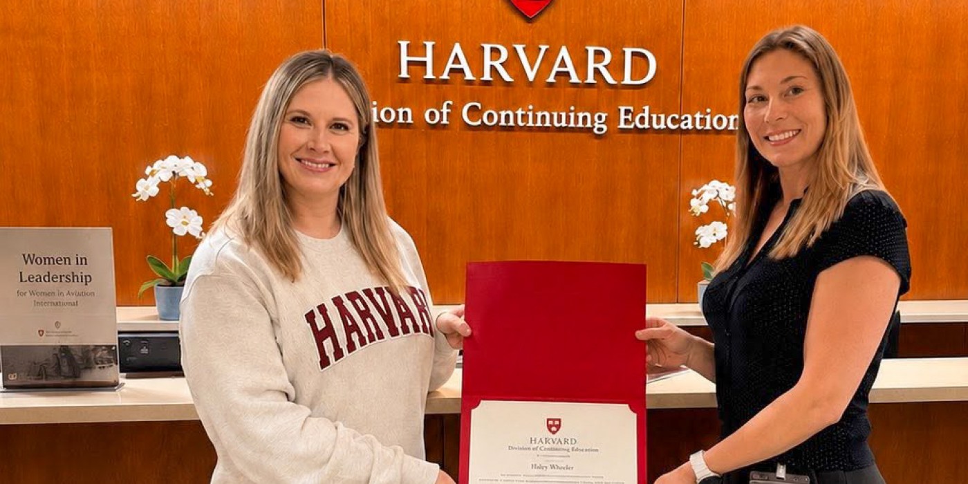 Two women smile while holding a certificate with Harvard University's logo