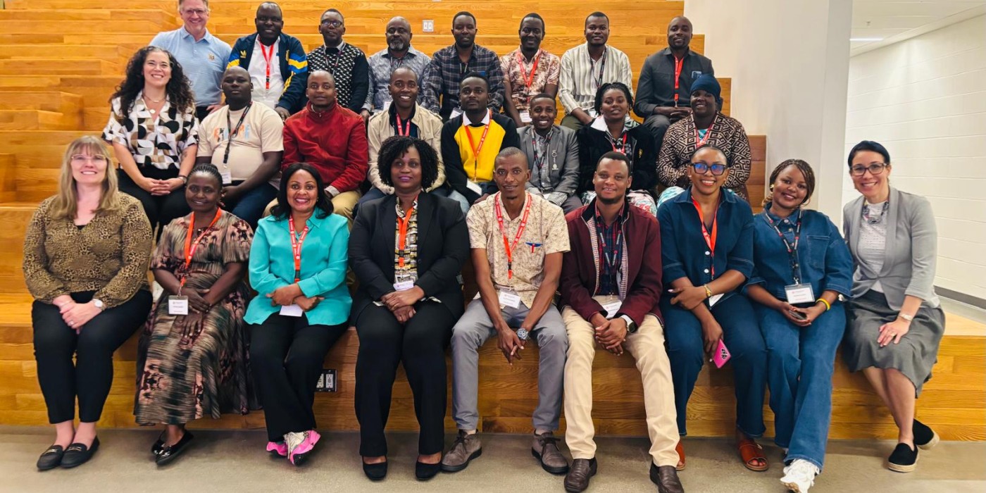 A large group of Tanzanian educators and Fanshawe Global representatives pose together on tiered wooden seating in a modern indoor space.
