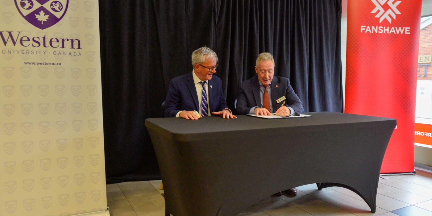 Western President Alan Shepard and Fanshawe President Peter Devlin sit at a table signing a partnership agreement.