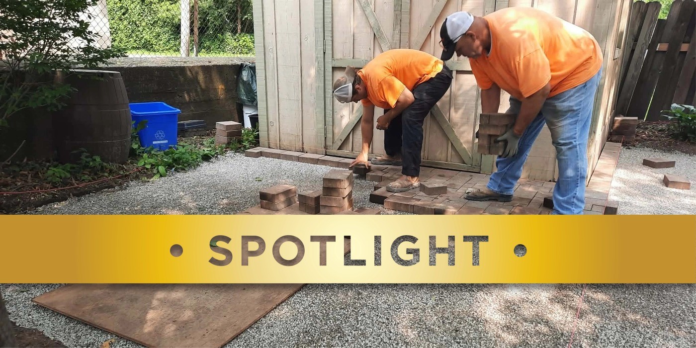 Two people in orange shirts laying down bricks on a patio.