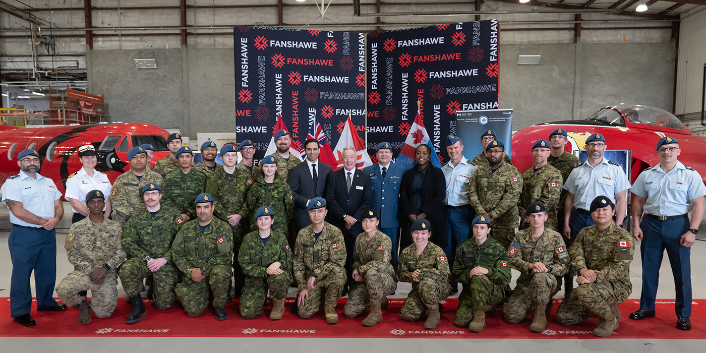 A large group of people in military uniforms and business attire stand in front of two red aircraft