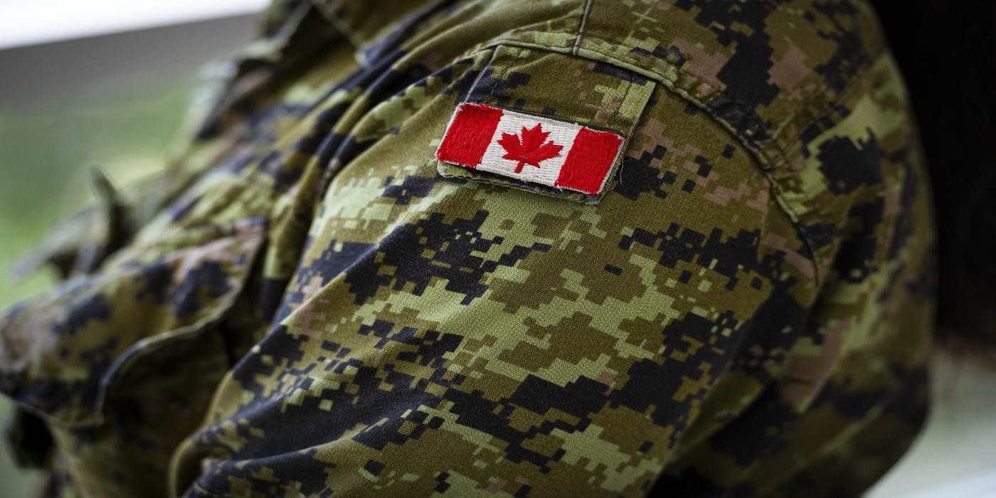 A close-up of a camouflage jacket with a Canadian flag patch on the upper arm.