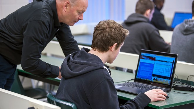 Teacher helping student with coding on computer
