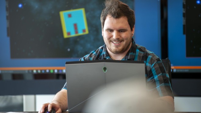 Game development student, on laptop and in front of multiple screens, presenting his work