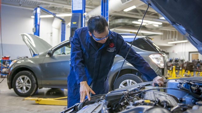 Student in automotive lab, looking under hood of car
