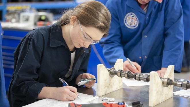 Automotive Service Technician student writing at a table in an automotive lab