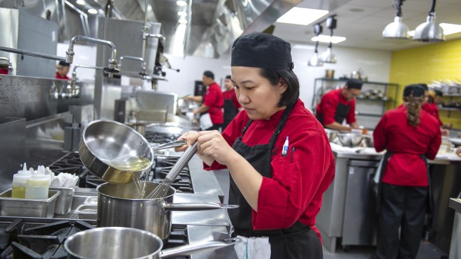 Culinary student pouring liquid into pot on stove in culinary lab