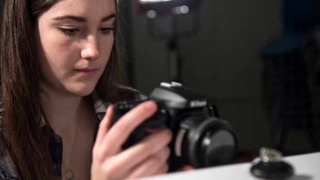 Girl with camera taking photo of small object in studio