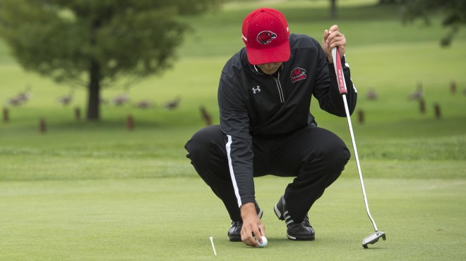 Person with golf club, on golf course, bending over to place ball on green
