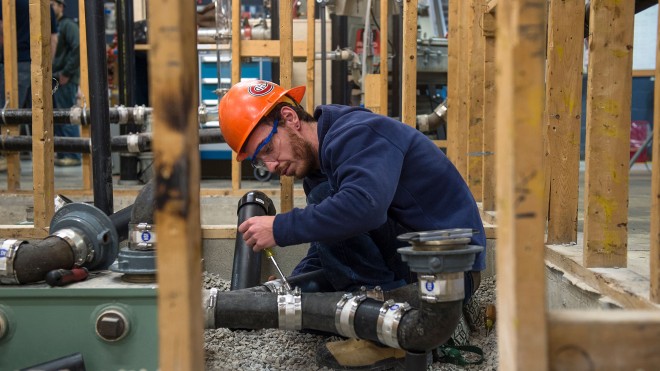 Plumbing student tightening pipes in construction setting