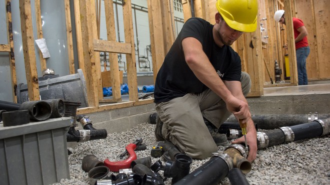Plumbing student tightening pipes in construction setting