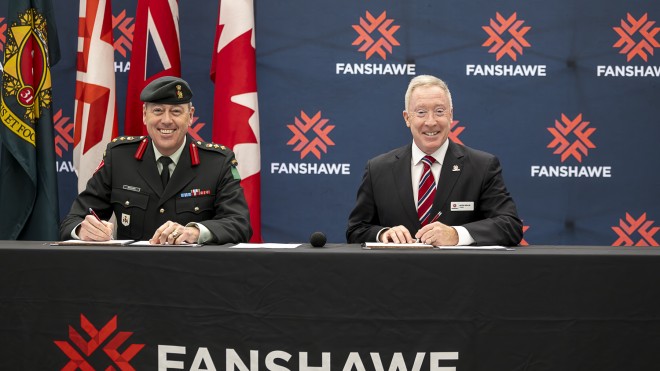 Colonel Chris Brown and President Peter Devlin seated at a table in front of Fanshawe backdrop to sign an MOU agreement.