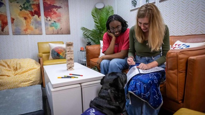 two students sit together in the Kind Space at Fanshawe, working with Heartley, the facility's dog for Canine Assistance Intervention