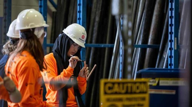 a person wearing a hard hat and safety glasses uses a small brush on a copper pipe