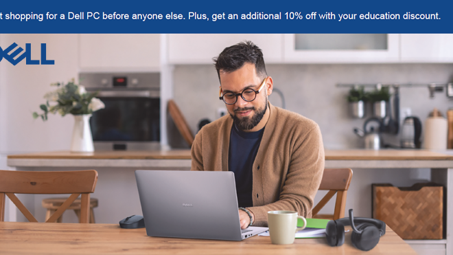 A man smiling and working on a laptop in a bright kitchen