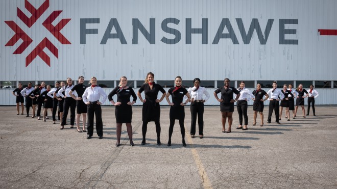 Faculty and students from the Flight Services program line up in uniform in front of the large sliding doors to the hangar which is decorated in a huge Fanshawe logo