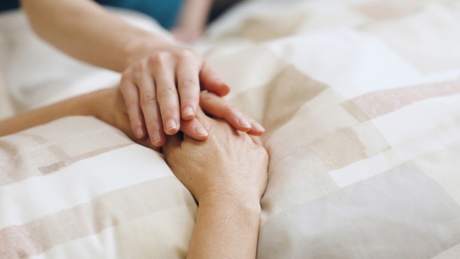 A comforting hand rests gently on another's, conveying empathy and support. The hands lie on a patterned beige blanket, suggesting a serene atmosphere.