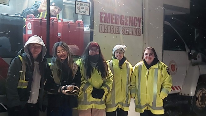 Five people in reflective coats in front of a white truck in the snow