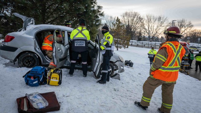 Paramedic students participate in a simulation at Fanshawe College's London Campus, responding to a car accident in snowy conditions, with emergency personnel and equipment visible.