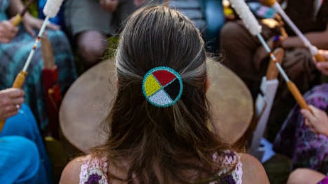 A woman in a drum circle is wearing a headband depicting the Indigenous medicine wheel.
