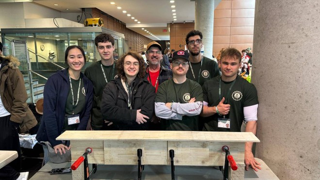 Seven students dressed in black stand behind a bridge they built using toothpicks, glue and dental floss.