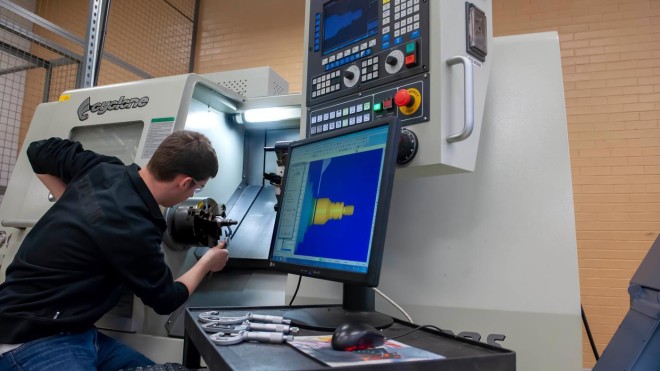 Inside a Fanshawe College lab, a Cyclone machine is being operated, with a computer screen displaying a 3D model.