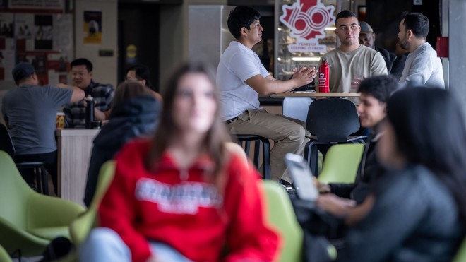 Student sitting on chairs and at tables in a student lounge area.