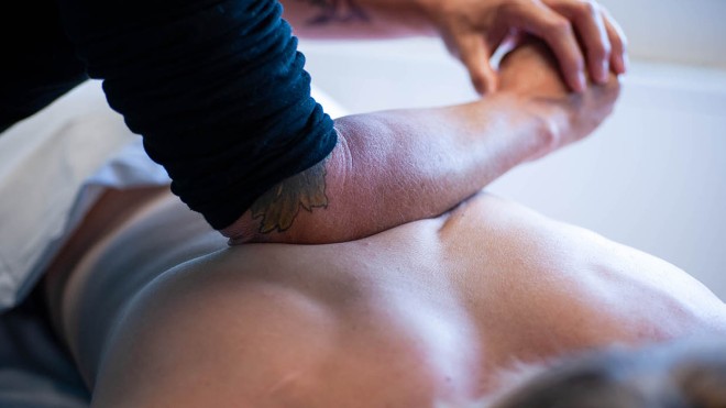 At the School of Health Sciences of Fanshawe College at the London Campus, a person lies on their stomach on a white surface, while another person uses their elbow to apply pressure to their back.