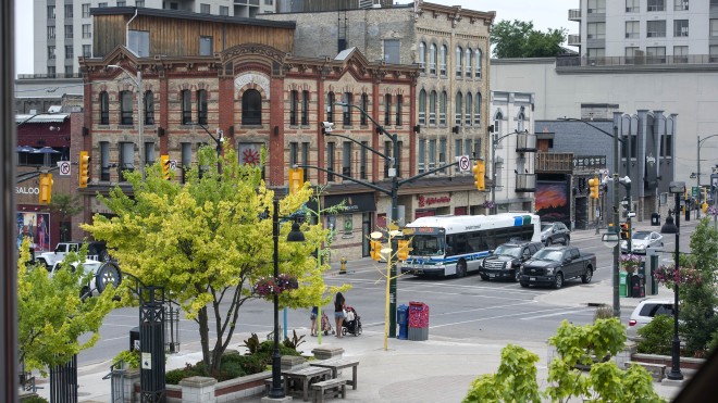 A view from a window overlooking a city street, where people are walking and vehicles are navigating the intersection, showcasing the urban environment and daily life.
