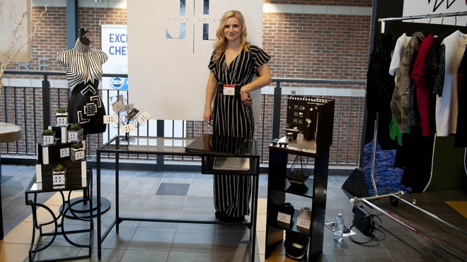 At the London Campus of Fanshawe College, a person stands in front of a display for the Fashion Marketing and Management program, featuring a banner with a logo, a mannequin, miniature displays, and a clothing rack.