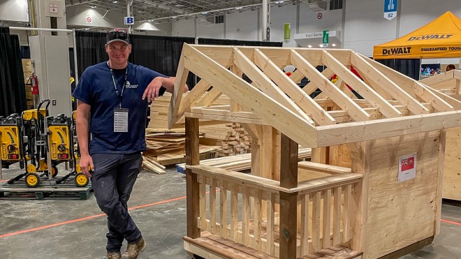 A carpentry apprentice stands next to a small structure he built during Skills Canada competition.
