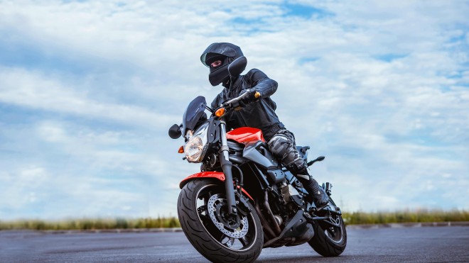 A person in black riding a red motorcycle on a cloudy day