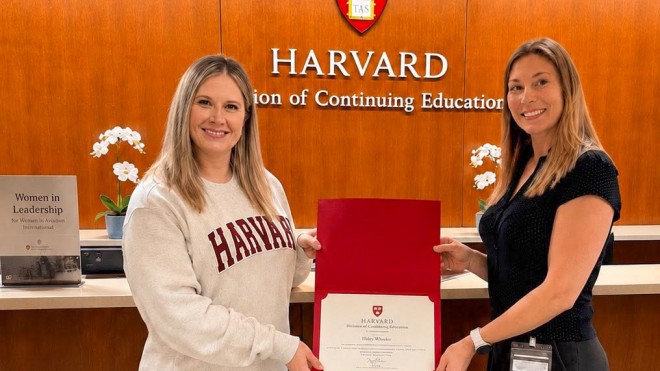 Two women smile while holding a certificate with Harvard University's logo