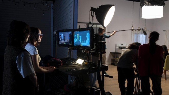 At Fanshawe College's London Campus, individuals are working on a Broadcasting - Television and Film Production set, with two monitors displaying the scene being filmed in a kitchen setting, while others operate lighting and sound equipment.