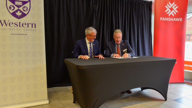 Western President Alan Shepard and Fanshawe President Peter Devlin sit at a table signing a partnership agreement.