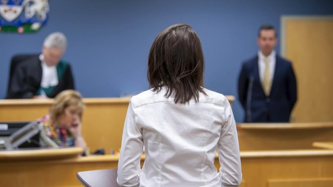 Inside the School of Public Safety at Fanshawe College's London Campus, a courtroom setting for the Paralegal program features a person standing at a podium, facing a judge's bench with two people seated behind it, and another person standing in the background.