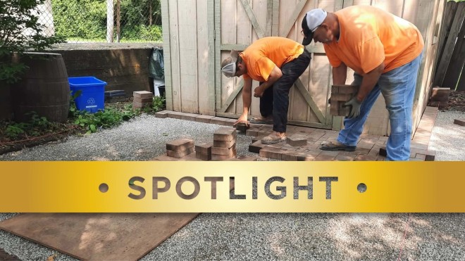 Two people in orange shirts laying down bricks on a patio.