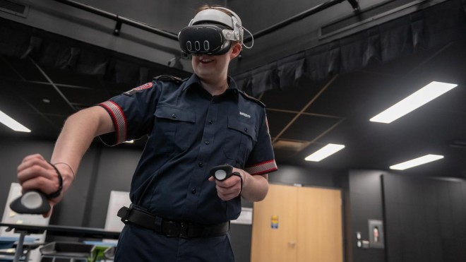 At the London Campus of Fanshawe College, a person wearing a Paramedic uniform and a VR headset holds controllers in both hands, in the Diane Blake Centre of Excellence in XR.