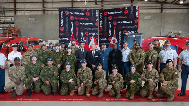 A large group of people in military uniforms and business attire stand in front of two red aircraft