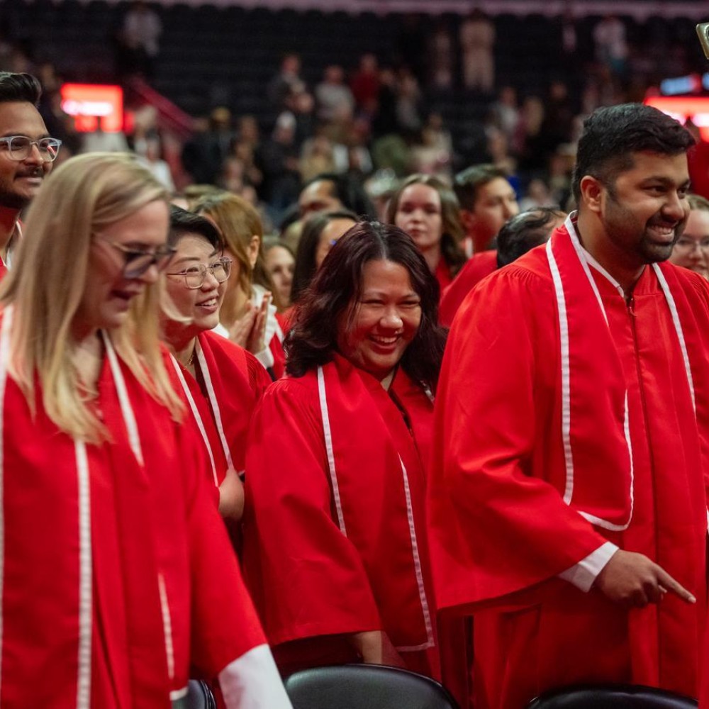 Fanshawe College graduates in red gowns smile during their convocation ceremony at Canada Life Place in London, Ontario.