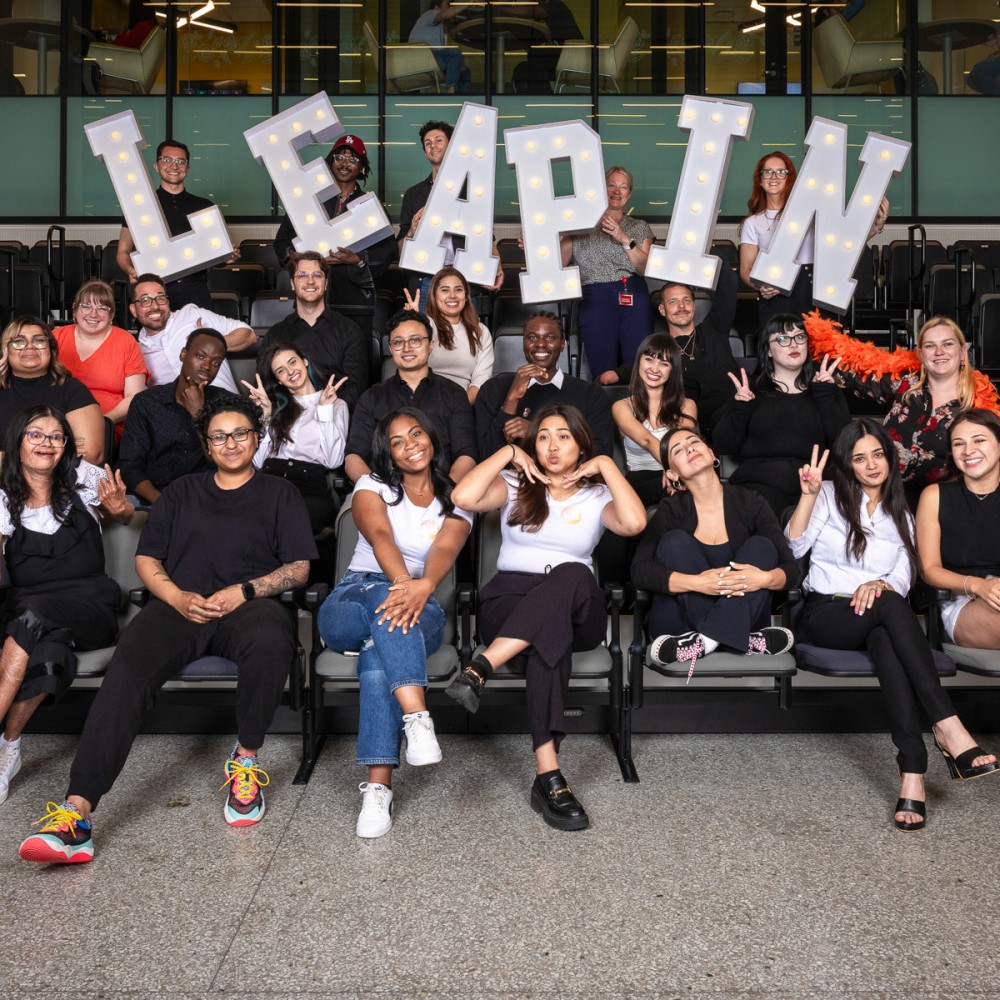 Group of students posing for a phot with a Leap In sign in the background