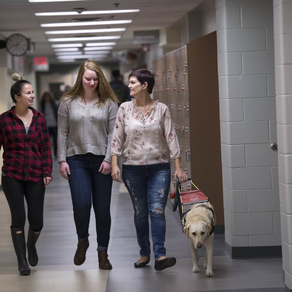 Three women walking in the hallway with a service dog