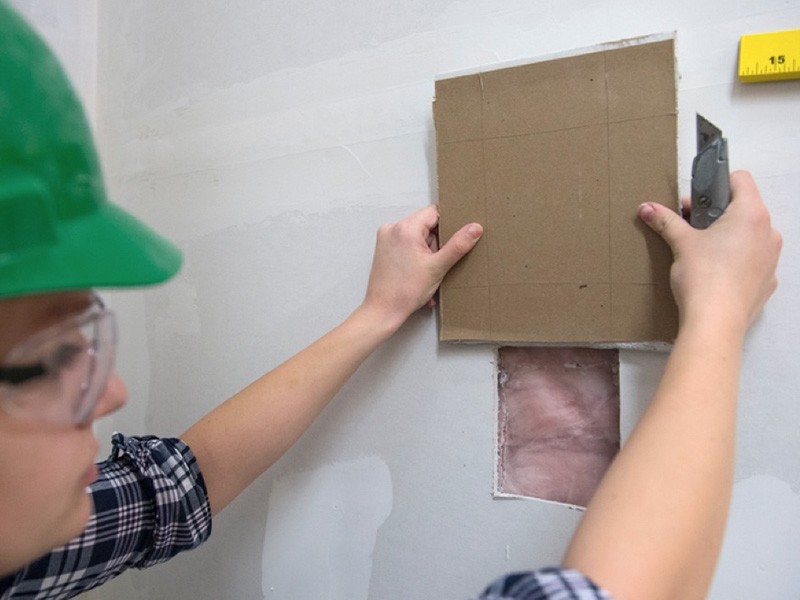 Student measures drywall patch. 