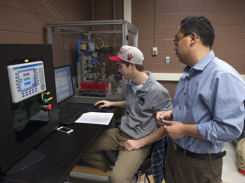 two people in front of electrical equipment and computer