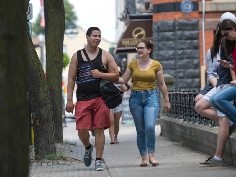 Students walking down a downtown street in the summer heat.