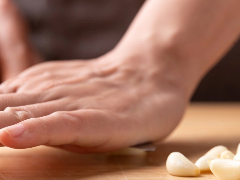 A palm placed on the flat size of a knife smashing garlic