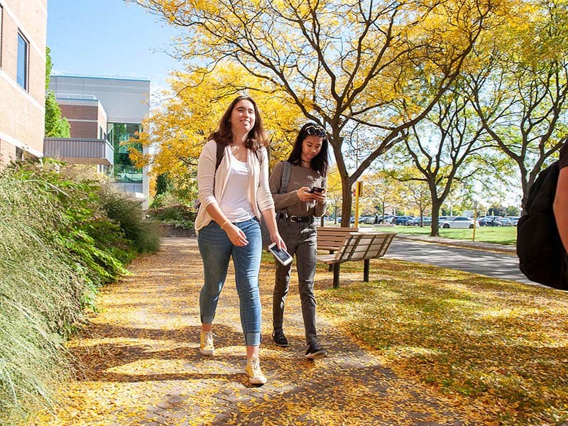 two women walking together down a sidewalk in fall
