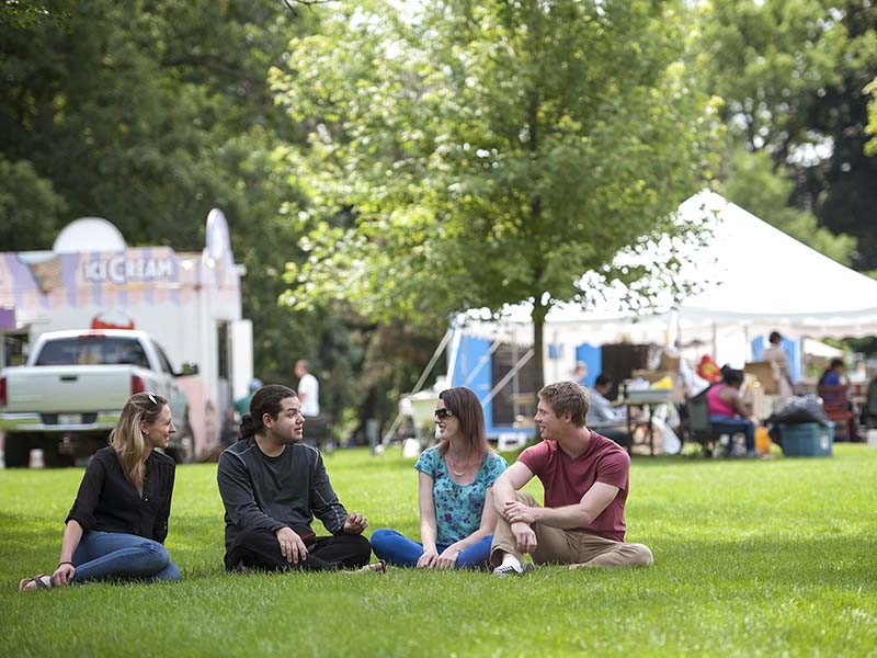 young people sitting on the grass in front of festival tents